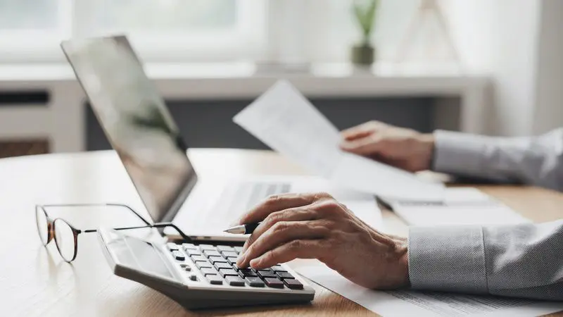 Person using calculator and laptop for accounting.